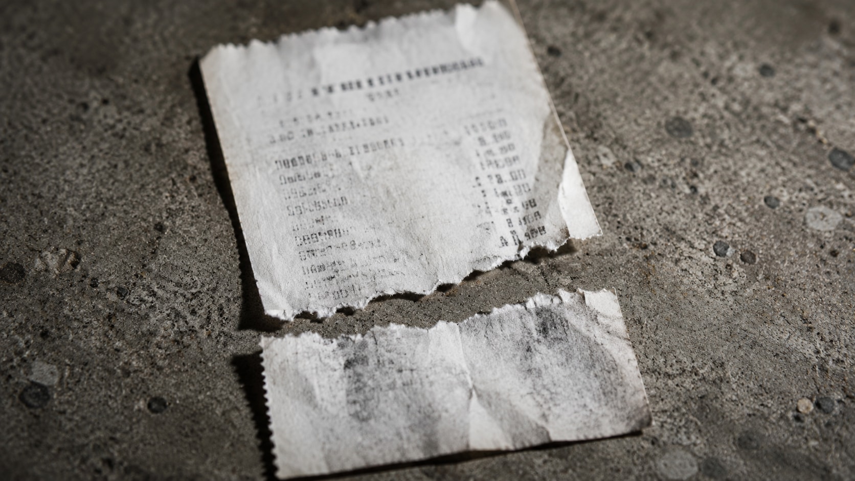 Must visibly show: a severely damaged thermal receipt torn completely in half. Local anchors: calidad de la imagen es intencionadamente destructiva, falta la mitad inferior donde figura el total, ningún modelo multimodal podrá inventar esos datos. Style family: material macro. Visual brief: A close up documentary shot of a severely damaged thermal receipt torn completely in half, missing the bottom total section. The torn paper rests on a raw concrete surface. Shot with a Sony A7R IV and a 90mm macro lens. Harsh directional lighting emphasizes the jagged torn edge and the faded, illegible ink. The image illustrates the physical limits of document recovery, with a shallow depth of field blurring the rough concrete background. Inline body image text firewall: visual content only. Do not render readable words anywhere. No article title, headline, subtitle, cover line, typography lockup, title card, poster text, labels, badges, UI copy, logo, brand name, or wordmark. If an interface, document, workflow, chart, or screen is needed, show abstract unreadable marks, shapes, icons, lines, and color blocks instead of words. Avoid repeating: robots looking confused, error screens on computers, people shrugging.